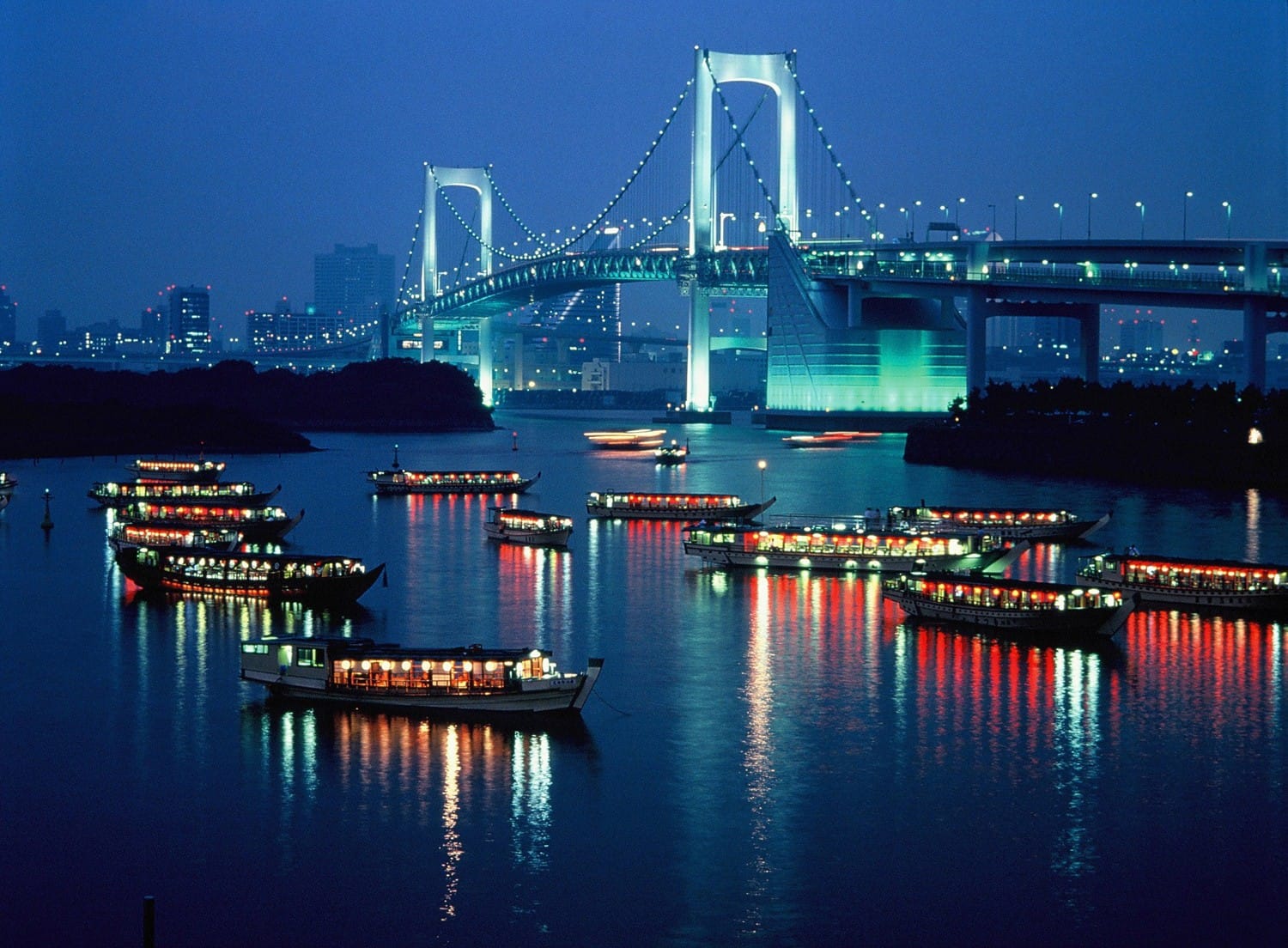 El Rainbow Bridge iluminado sobre la bahía de Tokio y barcos de recreo