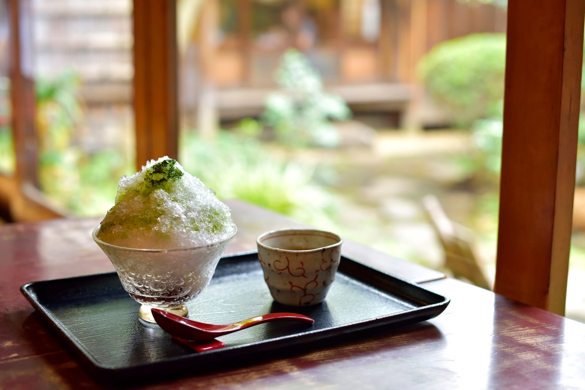 Un cuenco de hielo raspado con sirope verde junto a una taza de té