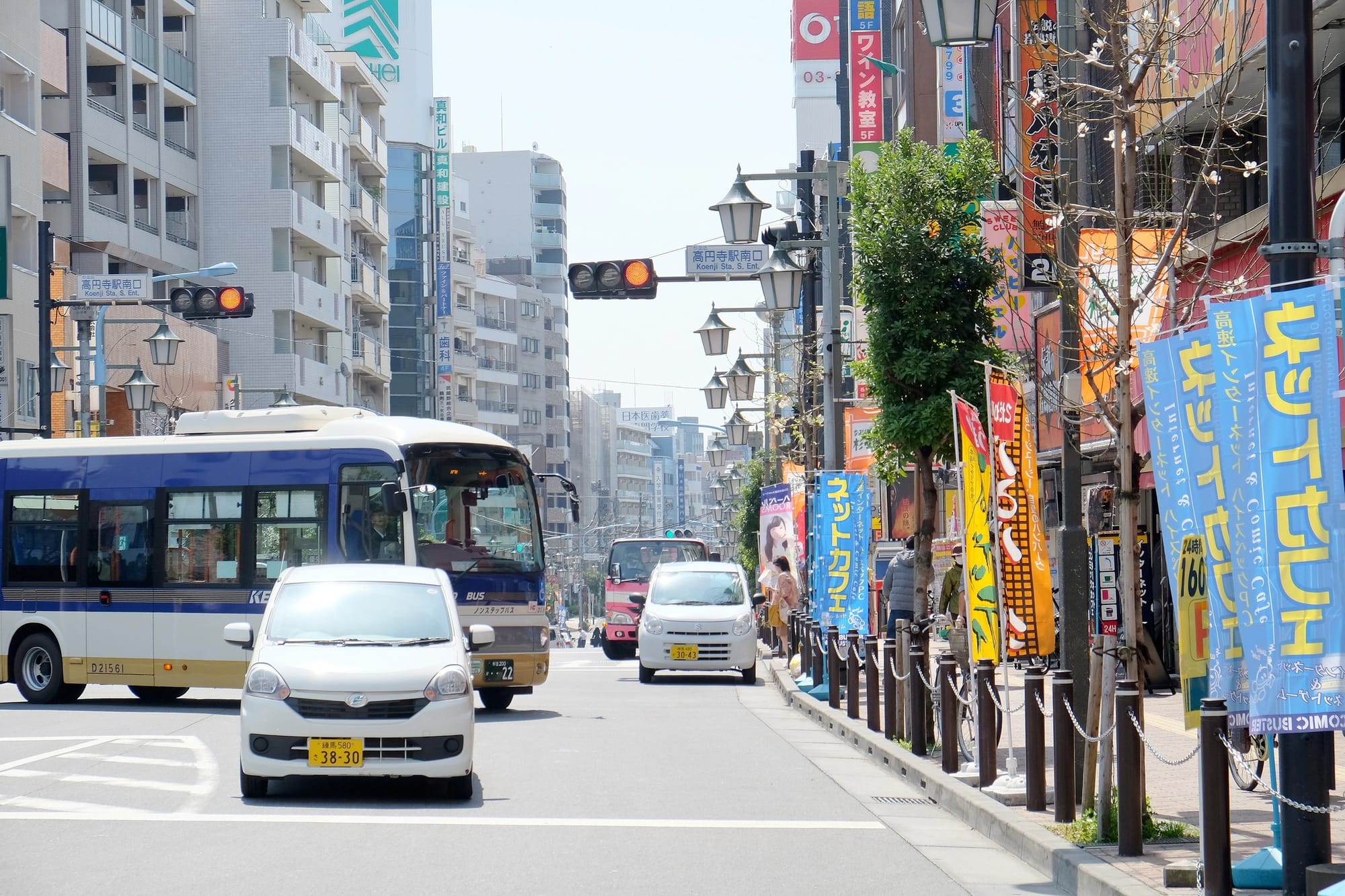 Una calle de Koenji con tiendas, vehículos y carteles comerciales