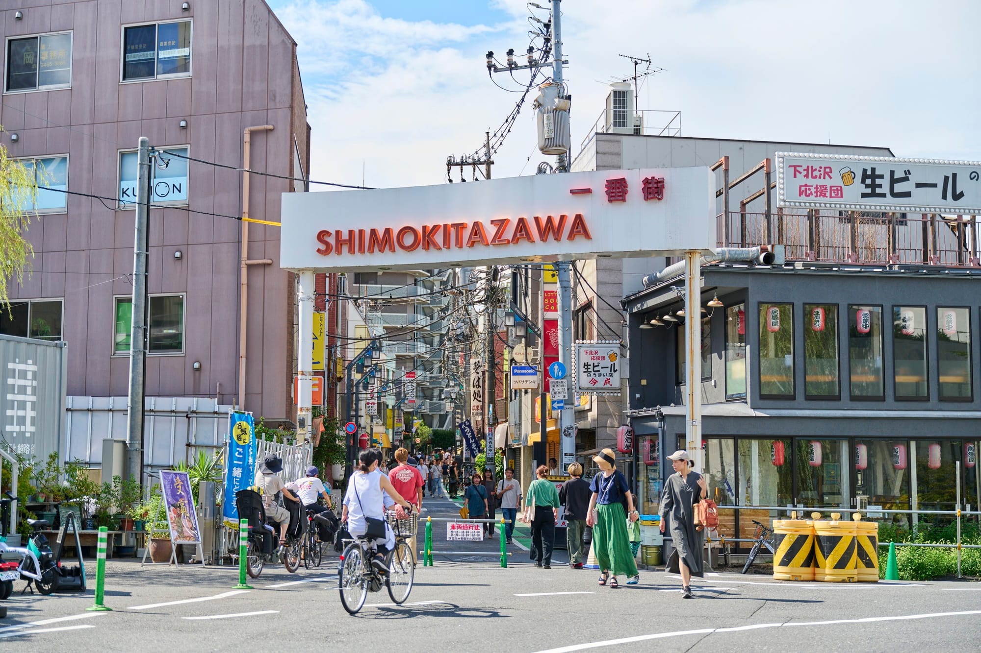 Entrada de una calle comercial de Shimokitazawa, con peatones y bicicletas
