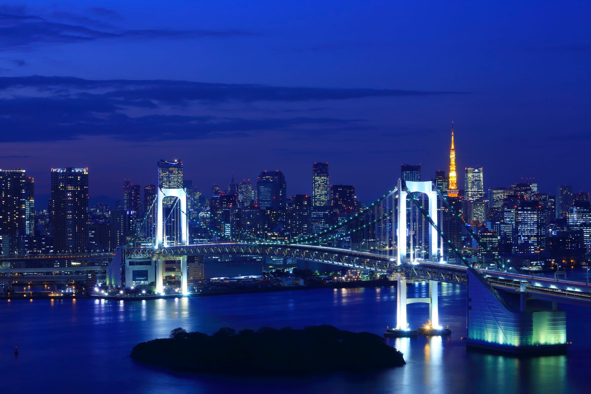 El Rainbow Bridge iluminado sobre la bahía de Tokio, con la torre de Tokio al fondo